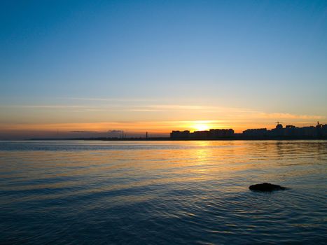 Sunset on a city thought bay with buildings silhouettes