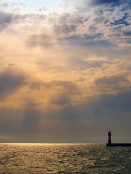 Sunset with visible sunrays in sea with lighthouse