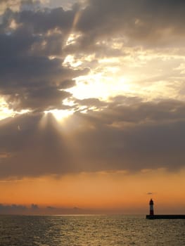 Sunset with visible sunrays in sea with lighthouse
