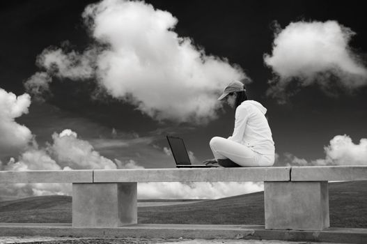 Woman working with a laptop sitting in a wall with a great view over a beautiful green meadow