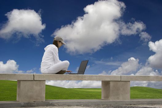 Woman working with a laptop sitting in a wall with a great view over a beautiful green meadow