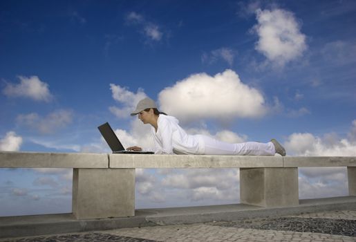 Woman working with a laptop sitting in a wall with a great view over a beautiful green meadow