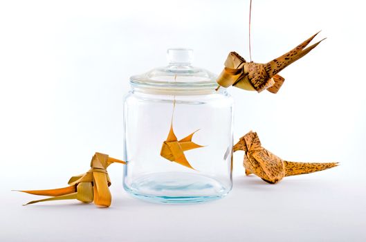 Leaf-made birds around a leaf-made fish in a glass jar.
