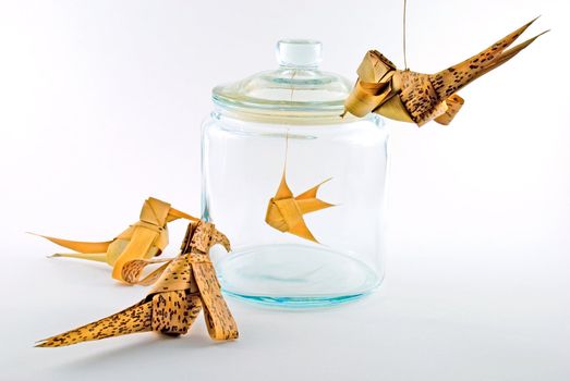 Leaf-made birds around a leaf-made fish in a glass jar.