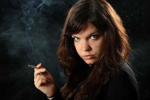 The beautiful girl smokes a cigarette against a dark background