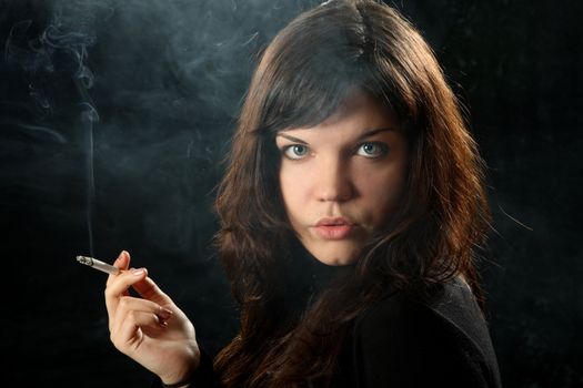 The beautiful girl smokes a cigarette against a dark background