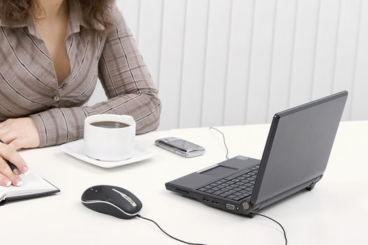 The young brunette at office with the laptop and coffee