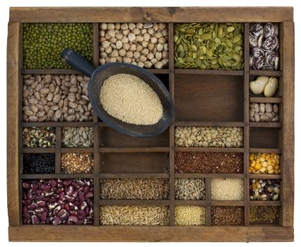 rustic scoop of amaranth grain and a variety of beans, lentils, seeds in old wooden typesetter case, isolated with clipping path