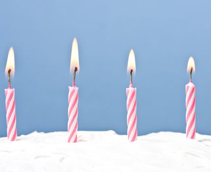 lit candles on a white frosted cake blue background