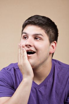 A young man with a surprised look on his face puts his hand on his cheek.