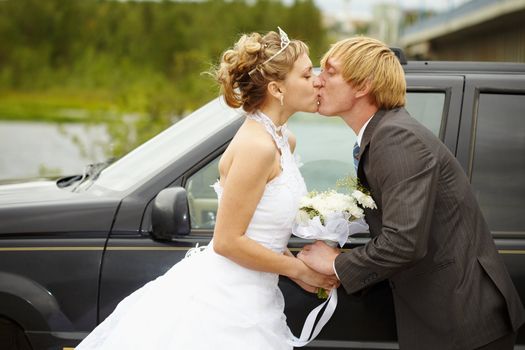 The bride and groom kissing near a black car