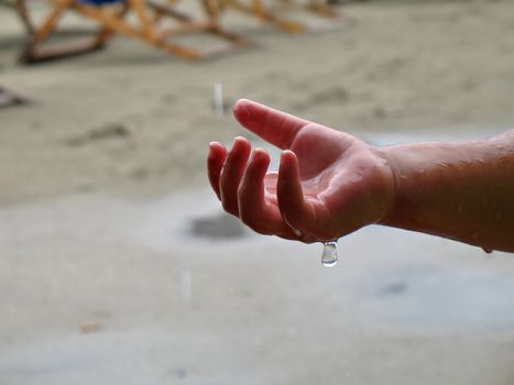 Child's hand is playing with rain drops at the end of summer season on the beach
