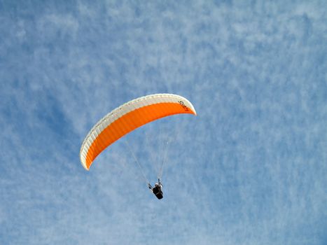 A paraglider il flying in the sky with his colourful paraglide