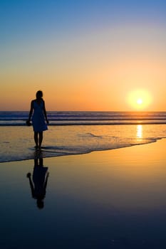 Woman walking on the beach at sunset.