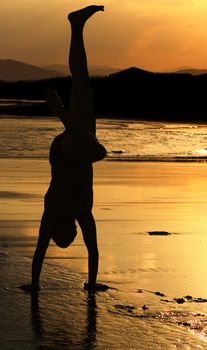 Silhouette of a man who makes a handstand on the beach at sunset