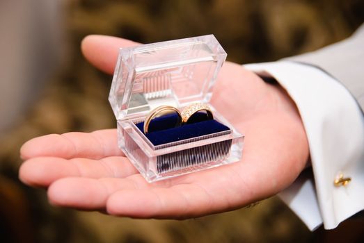 man's hand holding a transparent box with a wedding bands