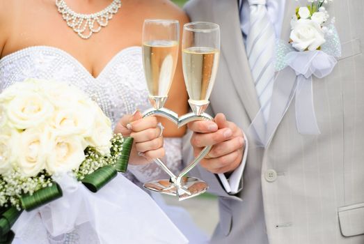 Bride and groom holding wedding heart-shaped glasses with champagne