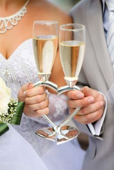 Bride and groom holding wedding heart-shaped glasses with champagne