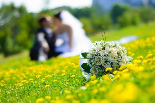 bridal bouquet of white roses on a green meadow and blurred newlyweds