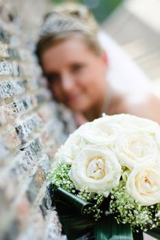 bridal bouquet of white roses and blurred bride near the wall at background