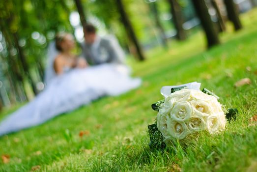 bridal bouquet of white roses on a green meadow and blurred newlyweds