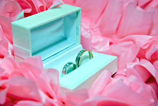 two wedding bands in a white box and pink ribbons at background