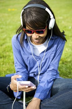 Black woman listening to the music in a park with white headphones