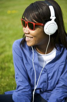 Black woman listening to the music in a park with white headphones