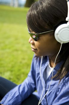 Black woman listening to the music in a park with white headphones