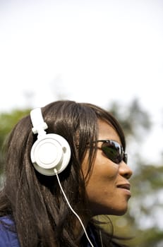 Black woman listening to the music in a park with white headphones