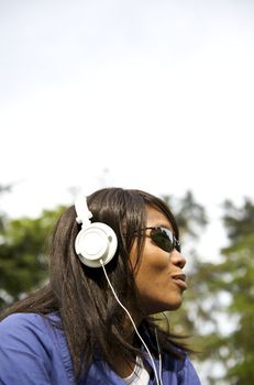 Black woman listening to the music in a park with white headphones