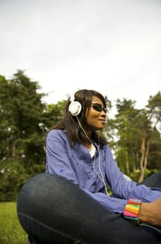 Black woman listening to the music in a park with white headphones