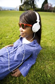 Black woman listening to the music in a park with white headphones