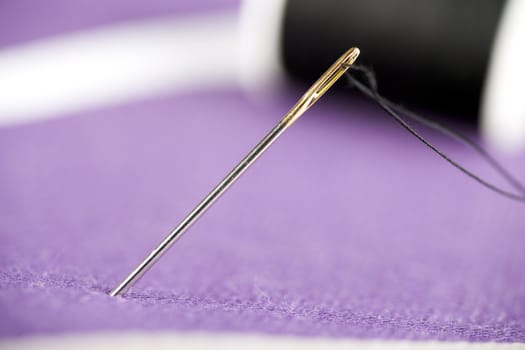 Threaded needle on purple fabric.
