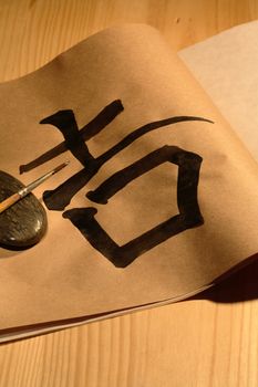 Paintbrush lying on black stone near paper with chinese symbol on wooden background