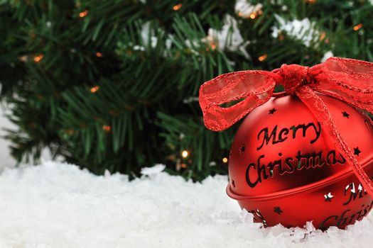 Beautiful red Christmas bell ornament lies in the snow with copyspace and a message of "Merry Christmas."