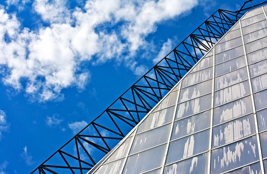 Glass wall of a greenhouse (conservatory) against blue sky and clouds