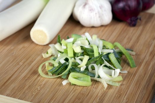 Sliced leeks with whole leeks, garlic and red onions in background.