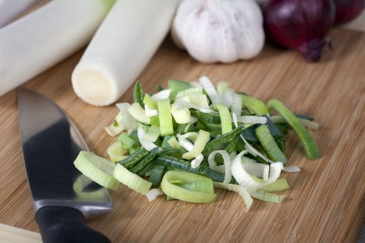 Sliced leeks with whole leeks, garlic and red onions in background.