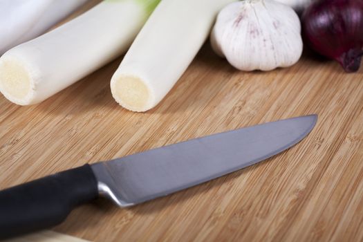 Knife on cutting board with vegetables in background.