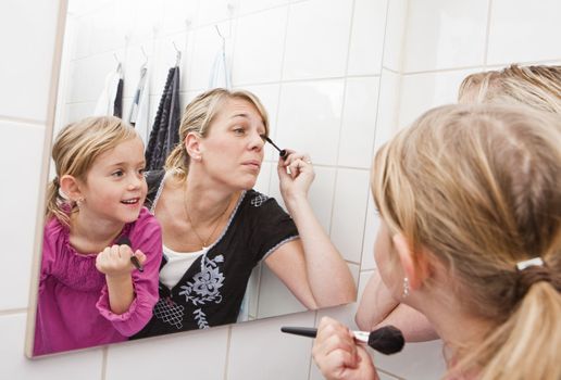 Mother and daughter put on make-up in the bathroom