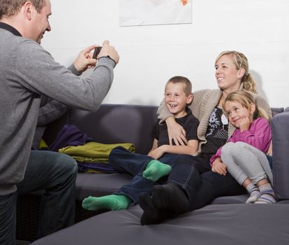 Father taking a photo of his family siting in the sofa