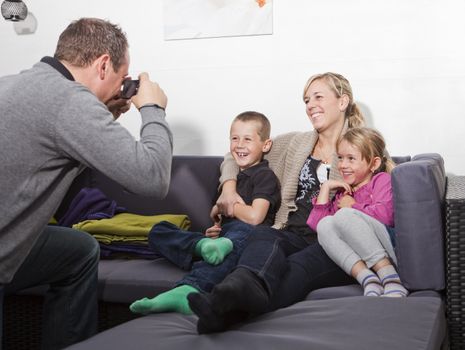 Father taking a photo of his family siting in the sofa