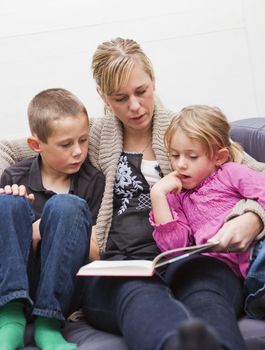 Mother in the sofa with her children reading a book