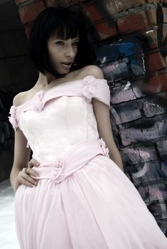 young bride in pink wedding dress standing among street ruins