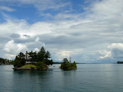 Two islands with a little bridge between and a cross on it and a house on the other between the thousand islands on the Ontario lake, Canada, by cloudy weather