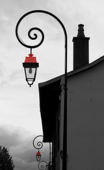 Old red lamps in a black and white photography of old buildings in a street by cloudy weather