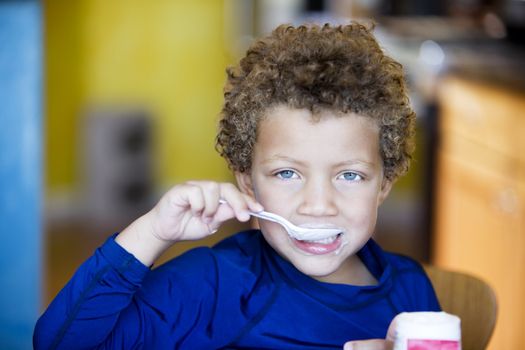 Handsome young boy with blue eyes eating yogurt