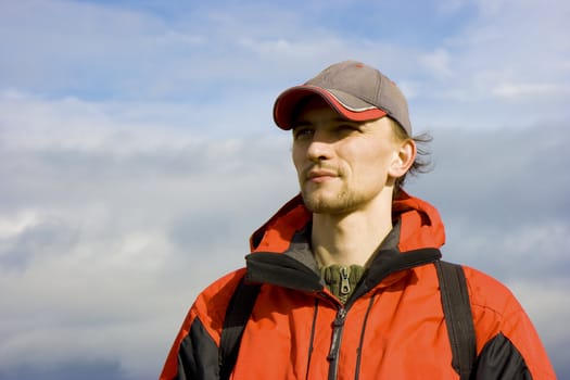 athletic young man in a cap against the blue sky with clouds
