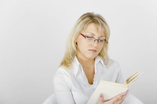 serious girl with glasses reading a book while sitting in a chair
